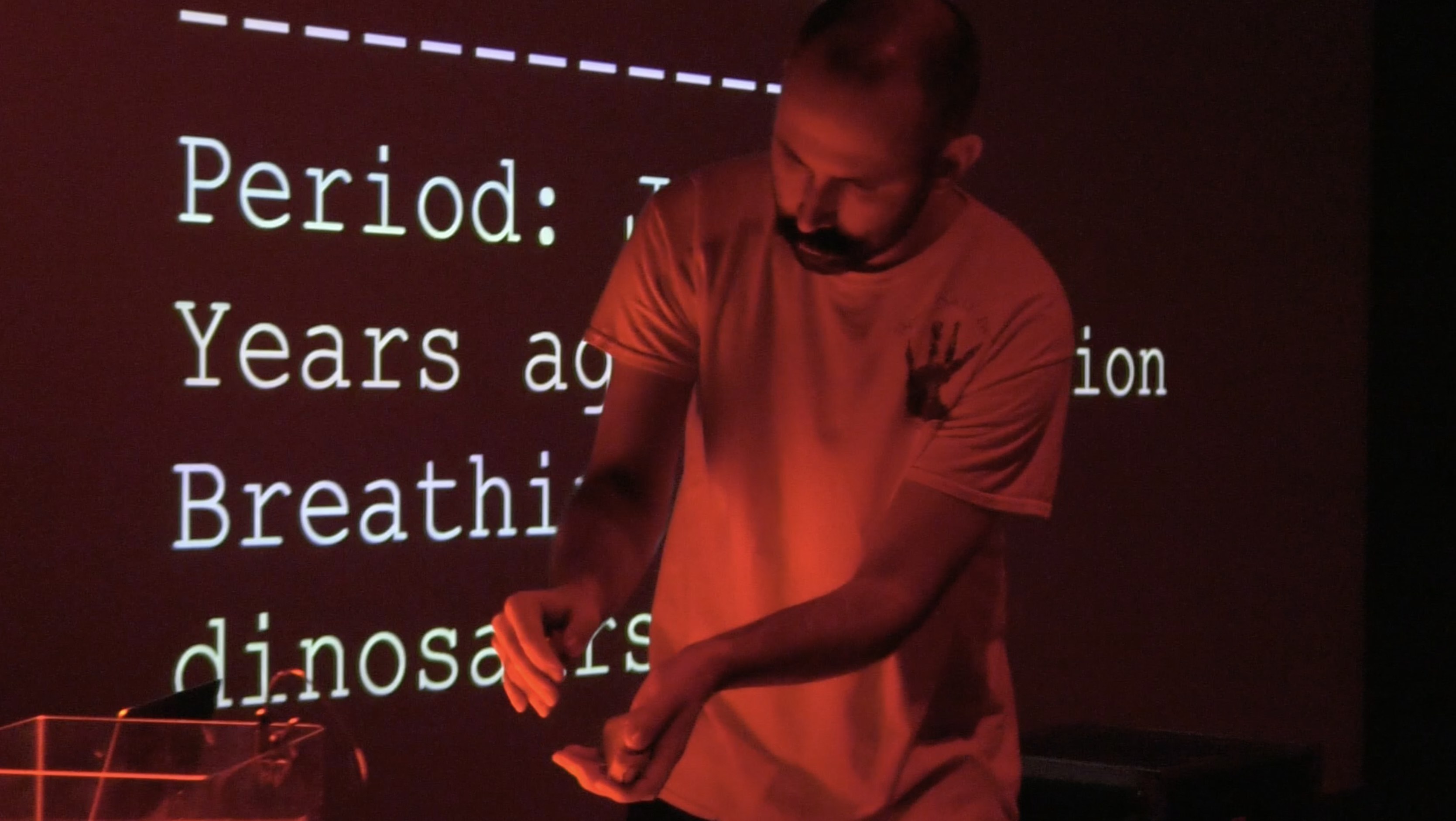 a mostly black, red, and white picture of Michael performing with one rock held in each hand. Each rock is embedded with a microcontroller.